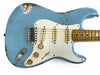 Close-up of vintage light blue electric guitar body with white pickguard, three single-coil pickups, volume and tone knobs, and worn maple fretboard showing relic wear and aging effects