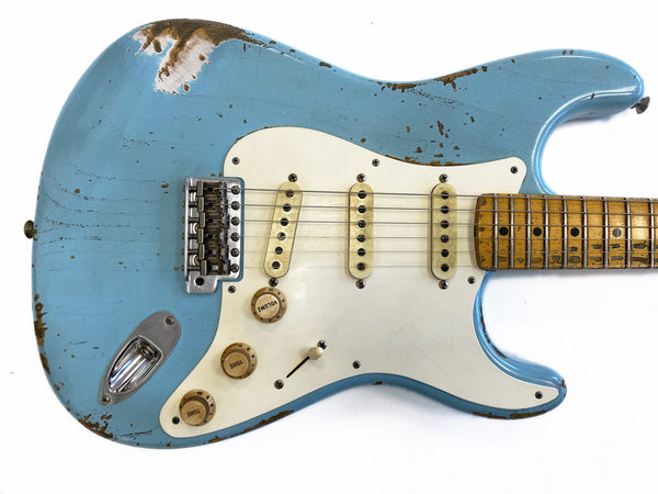 Close-up of vintage light blue electric guitar body with white pickguard, three single-coil pickups, volume and tone knobs, and worn maple fretboard showing relic wear and aging effects