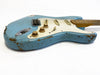 Close-up angled view of a vintage-style blue electric guitar with a distressed finish, white pickguard, three single-coil pickups, and three cream tone and volume control knobs on a white background.