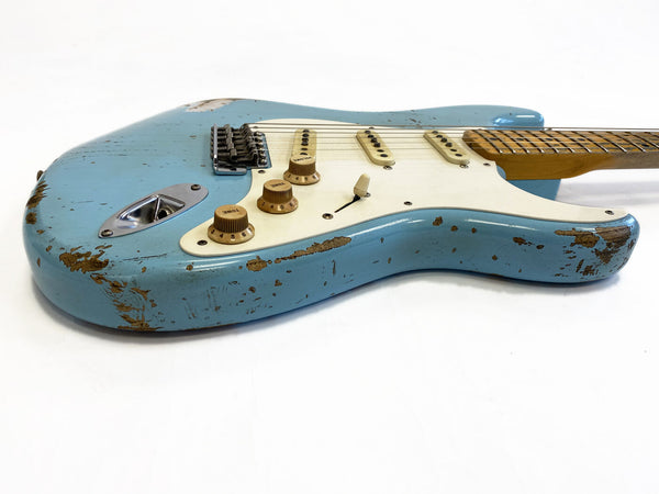 Close-up angled view of a vintage-style blue electric guitar with a distressed finish, white pickguard, three single-coil pickups, and three cream tone and volume control knobs on a white background.