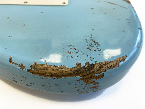 Close-up of vintage light blue electric guitar body with worn and chipped paint revealing wood grain beneath