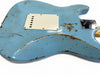 Close-up of worn light blue electric guitar body with relic finish, showing paint chips and scratches, white plastic backplate, and chrome neck plate screws