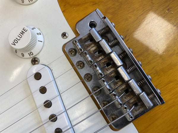 Close-up of Fender electric guitar bridge, strings, volume knob, and pickup on a worn yellow guitar body with white pickguard