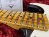 Close-up of vintage Fender electric guitar maple fretboard with aging yellow finish and metal frets, lying in red plush guitar case