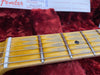 Close-up of worn maple guitar fretboard with metal frets and strings on Fender electric guitar neck in red plush case interior