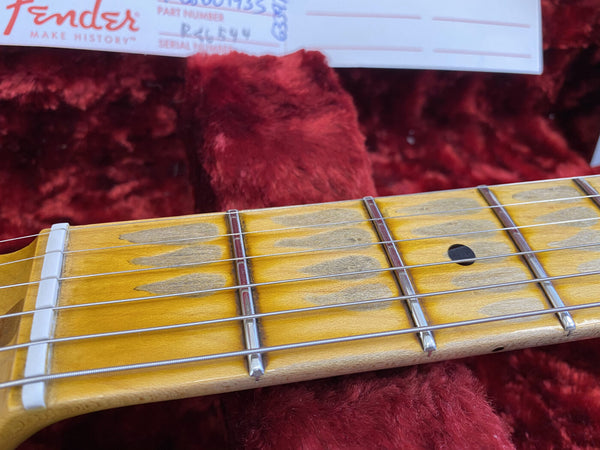Close-up of worn maple guitar fretboard with metal frets and strings on Fender electric guitar neck in red plush case interior
