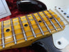 Close-up of worn maple guitar neck with metal frets and black dot inlays on electric guitar body with white pickguard and strings