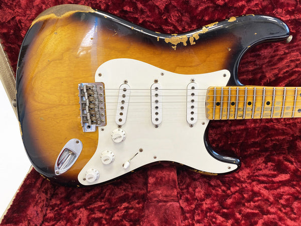 Vintage sunburst electric guitar with white pickguard, three single-coil pickups, and maple fretboard showing heavy wear and finish checking, resting on red plush guitar case lining