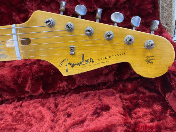 Close-up of vintage Fender Stratocaster guitar headstock with original contour body logo, six tuning pegs, and steel strings on red plush background
