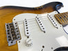 Close-up of vintage sunburst electric guitar body showing white pickguard, three single-coil pickups, volume knob, and worn maple neck with Fender branded bridge saddles