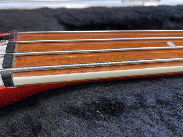 Close-up of bass guitar headstock showing metal strings, wooden fretboard, and black string nut on black fabric background