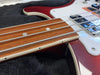 Close-up of red electric bass guitar neck, focusing on rosewood fretboard with silver strings and white dot inlays, lying on black fabric case interior.