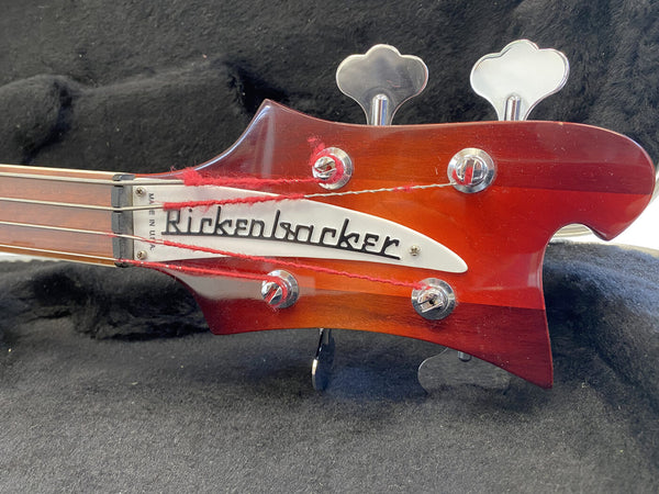 Close-up of Rickenbacker bass guitar headstock with tuning pegs and red strings on black fabric background