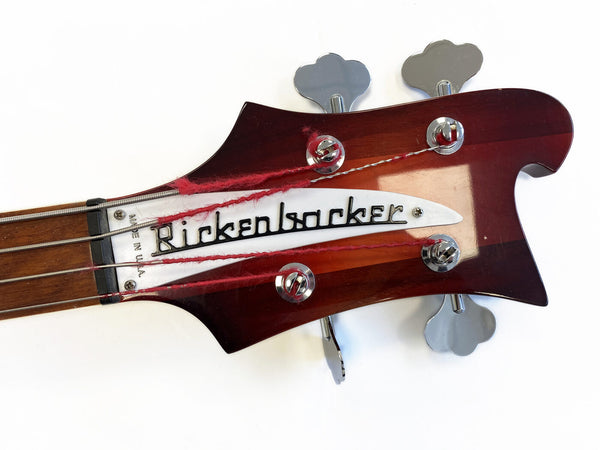 Close-up of vintage Rickenbacker bass guitar headstock with tuning pegs and red strings on white background