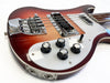 Close-up of a vintage electric bass guitar body with sunburst finish, featuring chrome bridge, pickup covers, black control knobs labeled for volume, tone, treble, and bass, and input jacks on a white pickguard.