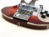 Close-up of red electric guitar body showing chrome bridge, strings, white pickguard, volume and tone knobs, and audio jack input on white background