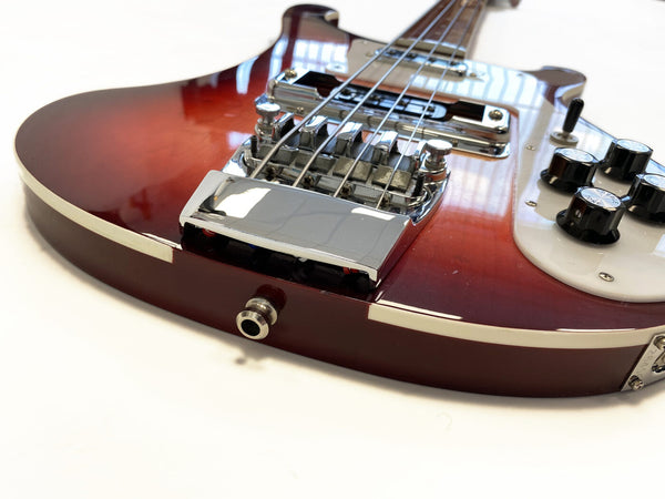 Close-up of red electric guitar body showing chrome bridge, strings, white pickguard, volume and tone knobs, and audio jack input on white background