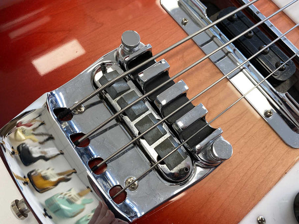 Close-up of chrome bridge and metal saddles on sunburst electric bass guitar with four strings and pickups