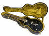 Black electric guitar with white pickups in open brown hardshell case with plush yellow interior lining on white background