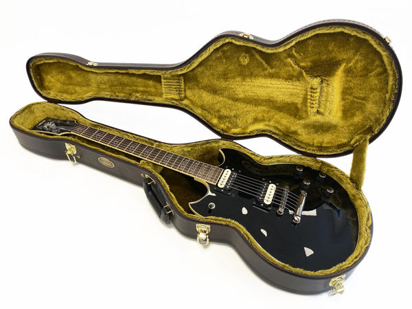 Black electric guitar with white pickups in open brown hardshell case with plush yellow interior lining on white background