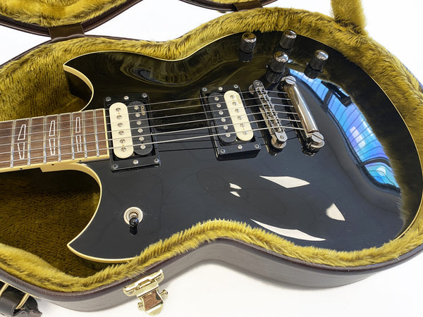 Black electric guitar with dual humbucker pickups and chrome hardware in a yellow plush-lined hard case