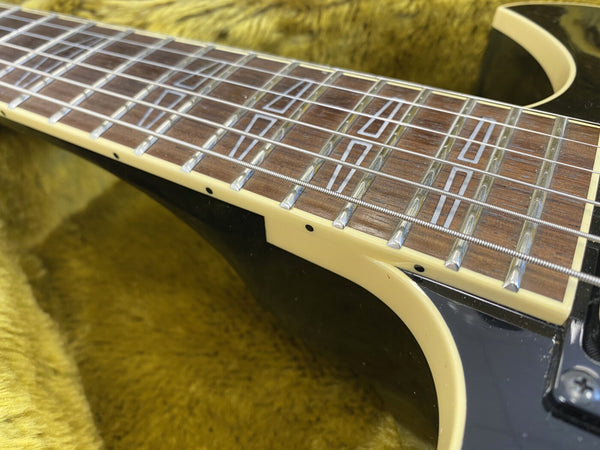 Close-up of electric guitar rosewood fretboard with trapezoid inlays, cream binding, and metal strings on black body with yellow plush background