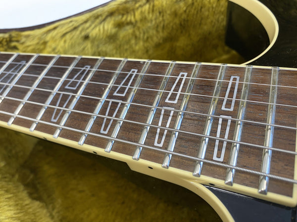 Close-up of guitar fretboard with rectangular inlays and metal strings on a wooden neck, guitar resting on yellow plush interior case lining