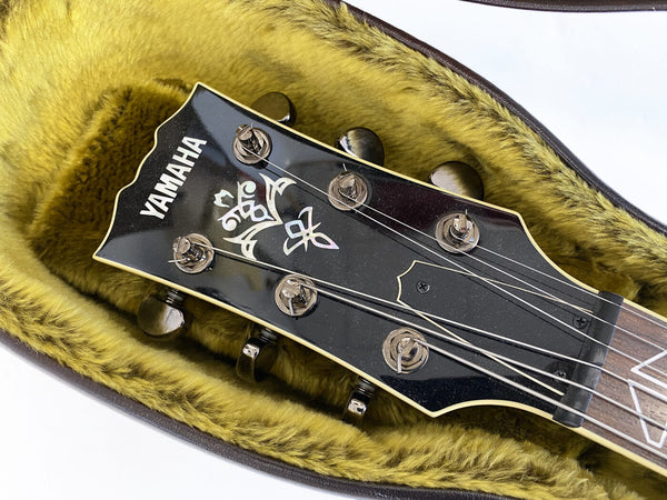 Close-up of Yamaha acoustic guitar headstock with tuning pegs and decorative inlay, resting in a plush yellow guitar case interior.