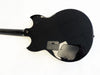 Back view of black electric guitar body showing battery compartment and control cavity cover against white background