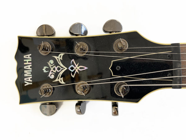 Close-up of Yamaha guitar headstock with tuning pegs, black finish, and decorative inlay on white background