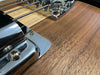 Close-up of guitar bridge and metal tailpiece on natural wood electric guitar body with chrome hardware and bass strings