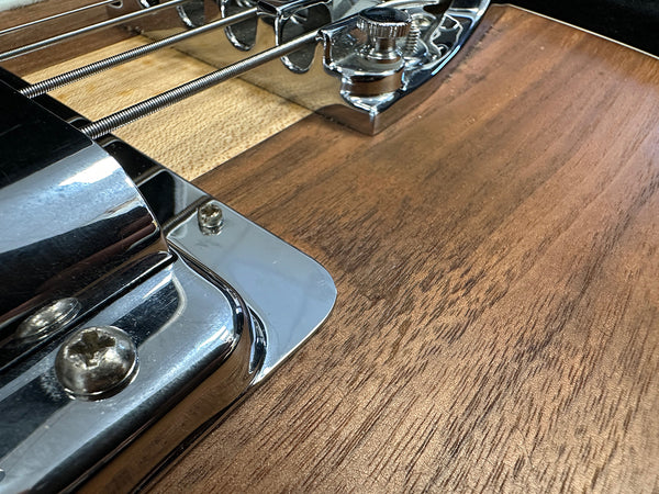 Close-up of guitar bridge and metal tailpiece on natural wood electric guitar body with chrome hardware and bass strings