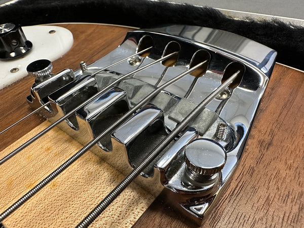 Close-up of electric bass guitar chrome bridge and metal strings on natural wood body