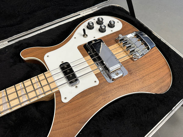 Electric bass guitar with natural wood finish, white pickguard, black control knobs, and chrome bridge hardware in black plush guitar case