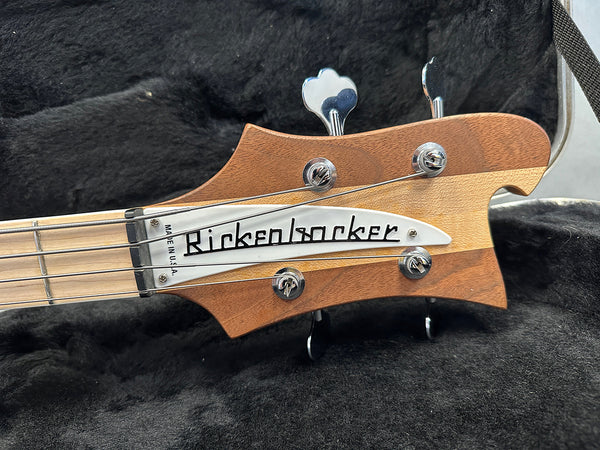 Close-up of Rickenbacker bass guitar headstock with wooden finish and chrome tuning pegs in a black padded guitar case