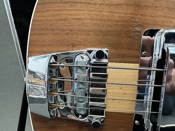 Close-up of chrome bridge and pickups on natural wood finish electric bass guitar with four strings and black strap