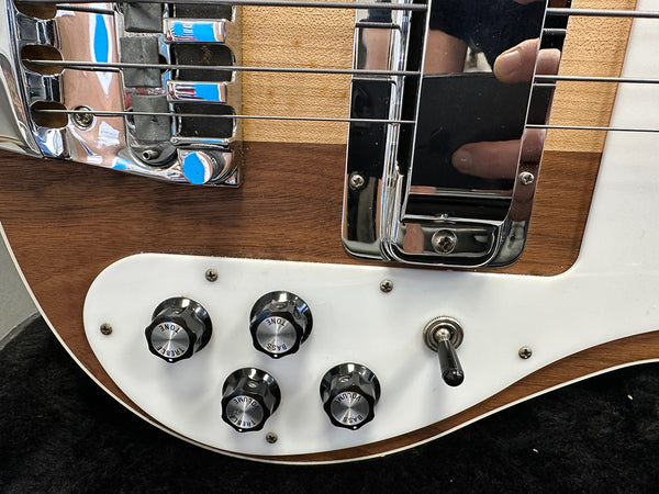 Close-up of electric bass guitar control knobs and bridge with chrome hardware on natural wood finish body