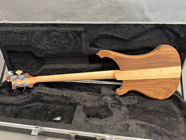 Back view of wooden electric bass guitar with natural finish in black plush lined hard case showing neck and headstock with tuning pegs