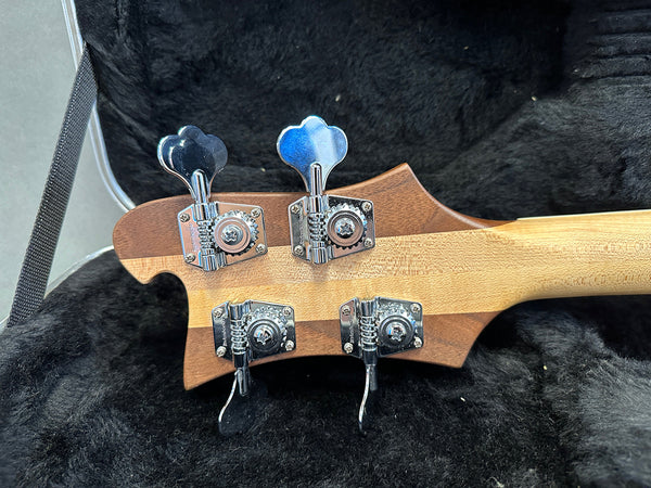 Close-up of bass guitar headstock with four chrome tuning pegs inside a black plush guitar case