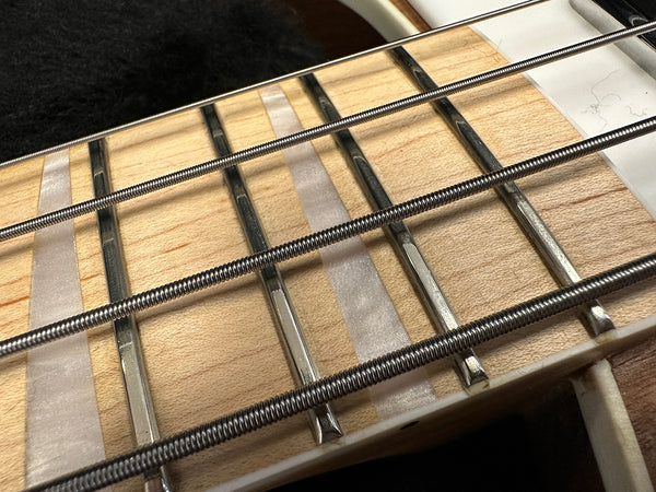 Close-up of bass guitar fretboard with metal frets, pearl inlays, and wound steel strings on light wood neck