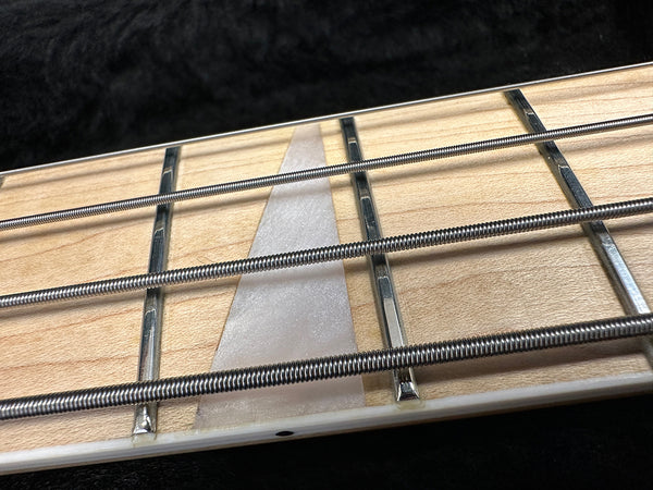 Close-up image of bass guitar fretboard showing metal frets, steel wound strings, and triangular inlay on light wood fingerboard