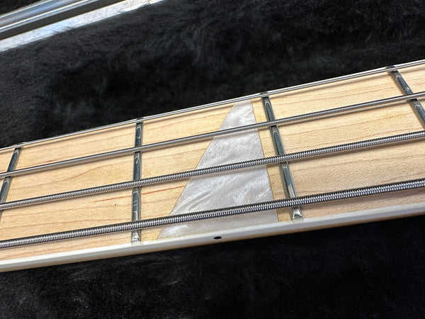 Close-up of maple guitar fretboard with silver frets, pearl inlay, and metal strings on black background