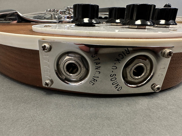 Close-up of vintage electric guitar output jack plate with "Rick-O-Sound" and "Stanco Inc" engraving, showing dual output jacks and black control knobs on wood finish guitar body