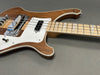 Close-up of natural wood electric bass guitar body and neck with white pickguard and triangular inlays on gray surface