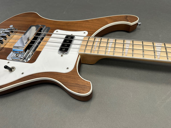Close-up of natural wood electric bass guitar body and neck with white pickguard and triangular inlays on gray surface