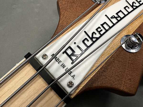Close-up of Rickenbacker bass guitar headstock with logo, tuning peg, and metal strings displayed on natural wood finish