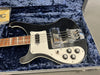 Black electric bass guitar with white pickguard and control knobs resting inside a blue plush lined hard case