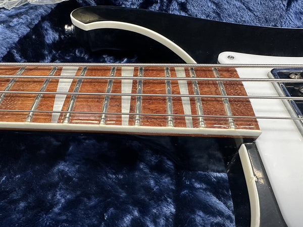 Close-up of four-string electric bass guitar fretboard with metal frets and wound strings on dark blue plush surface