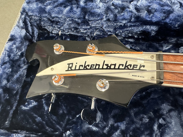 Close-up of black Rickenbacker bass guitar headstock with tuning pegs and strings, placed on blue plush guitar case lining, made in USA.