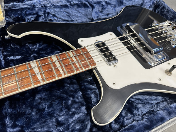 Close-up of black electric bass guitar with white pickguard and chrome hardware resting on blue plush case lining